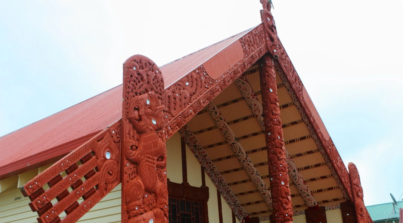 Carved red maihi and koruru of a wharenui in Rotorua, inlaid with pāua shell