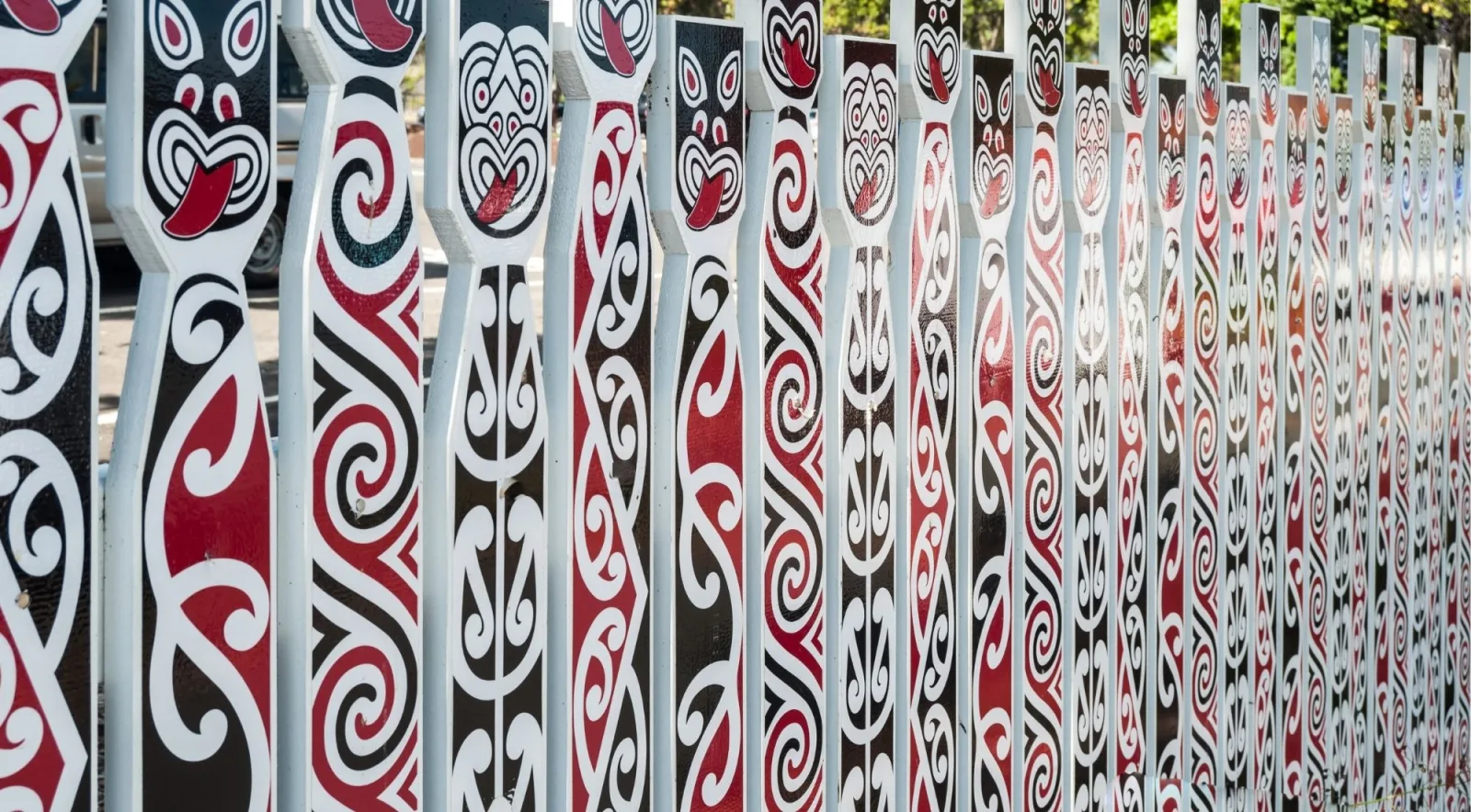 Painted palisade of carved Māori figures and kōwhaiwhai patterns in red, black and white