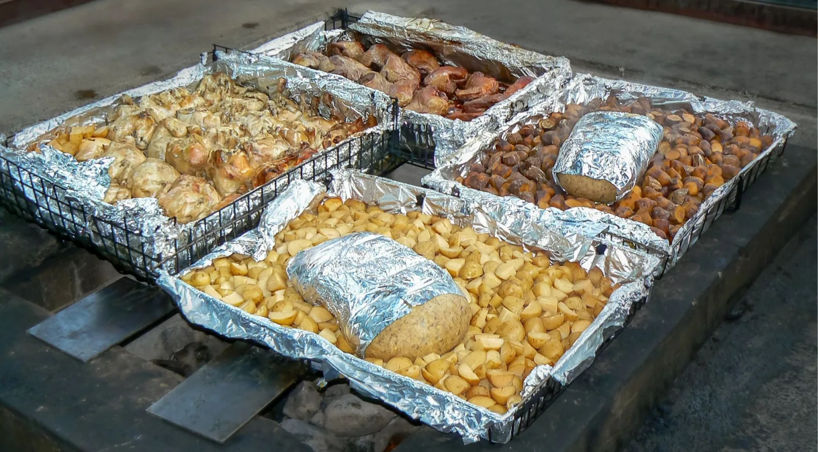 Foil-lined hāngī trays of pork, chicken, potatoes and kūmara lifted from the steam pit