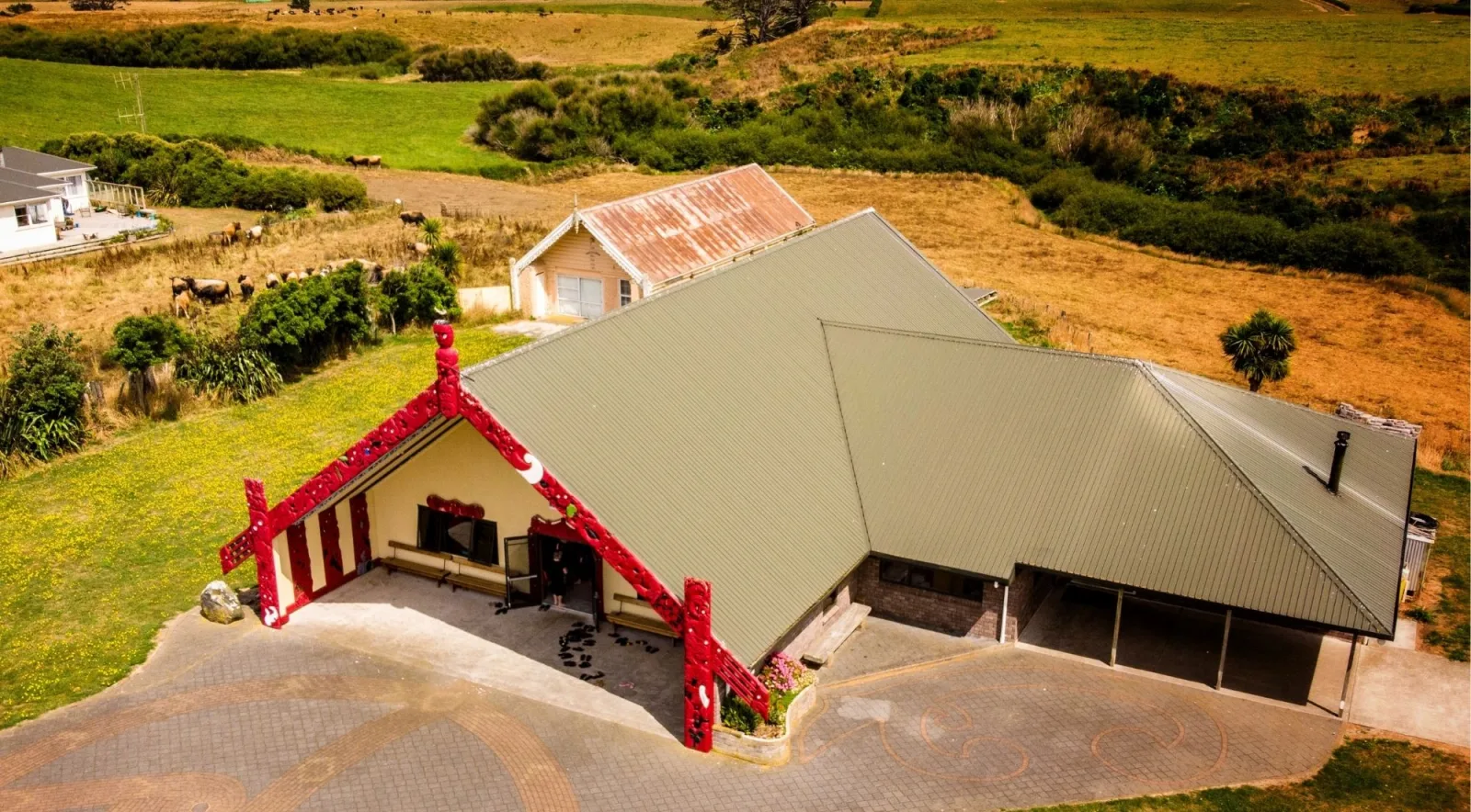 Aerial view of a carved wharenui and marae ātea surrounded by farmland