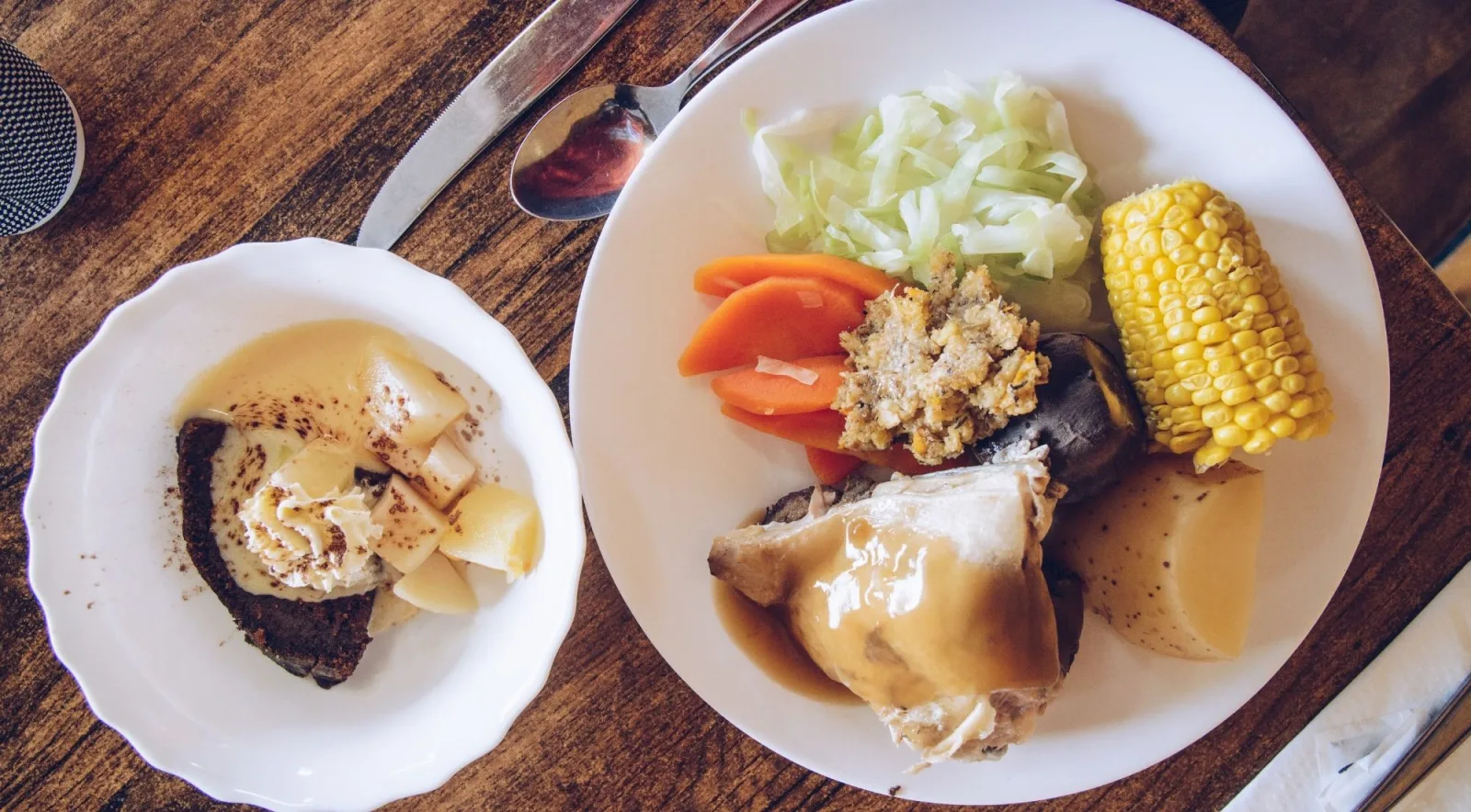 Plated hāngī dinner of chicken, corn, cabbage, carrot and kūmara beside a steamed pudding