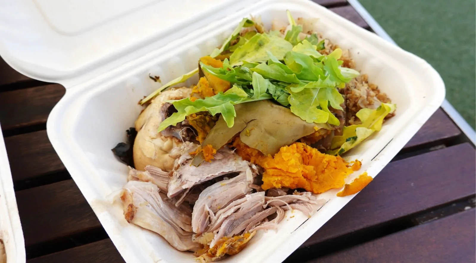 Hāngī box of shredded meat, mashed kūmara and puha greens on a picnic table