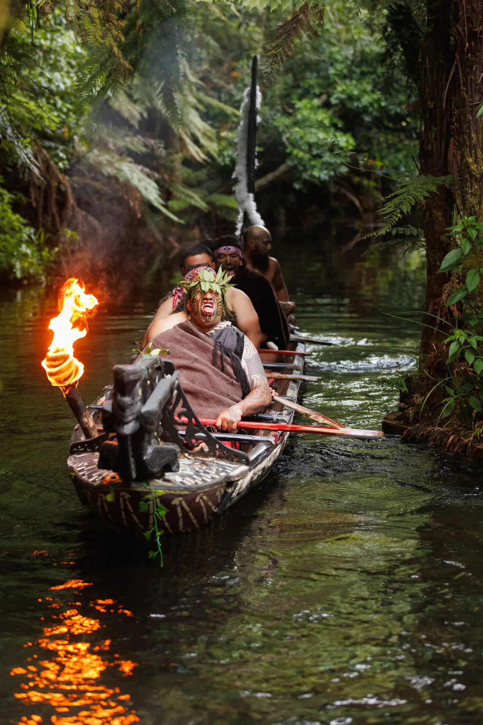 Warriors paddle a torch-lit waka down the Wai-o-whiro stream after dark at Mitai Māori Village