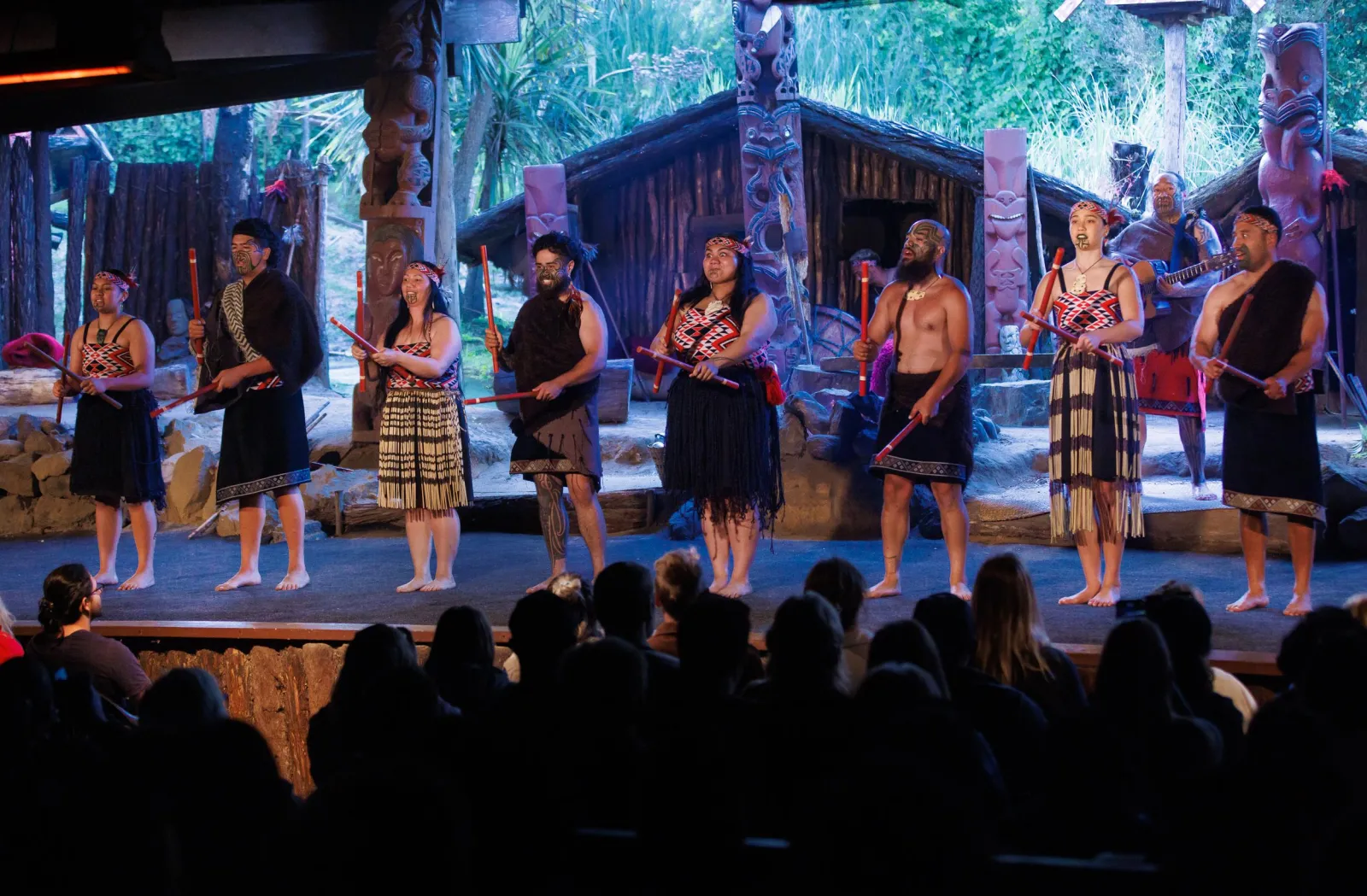 The full Mitai company performing in front of the carved village buildings