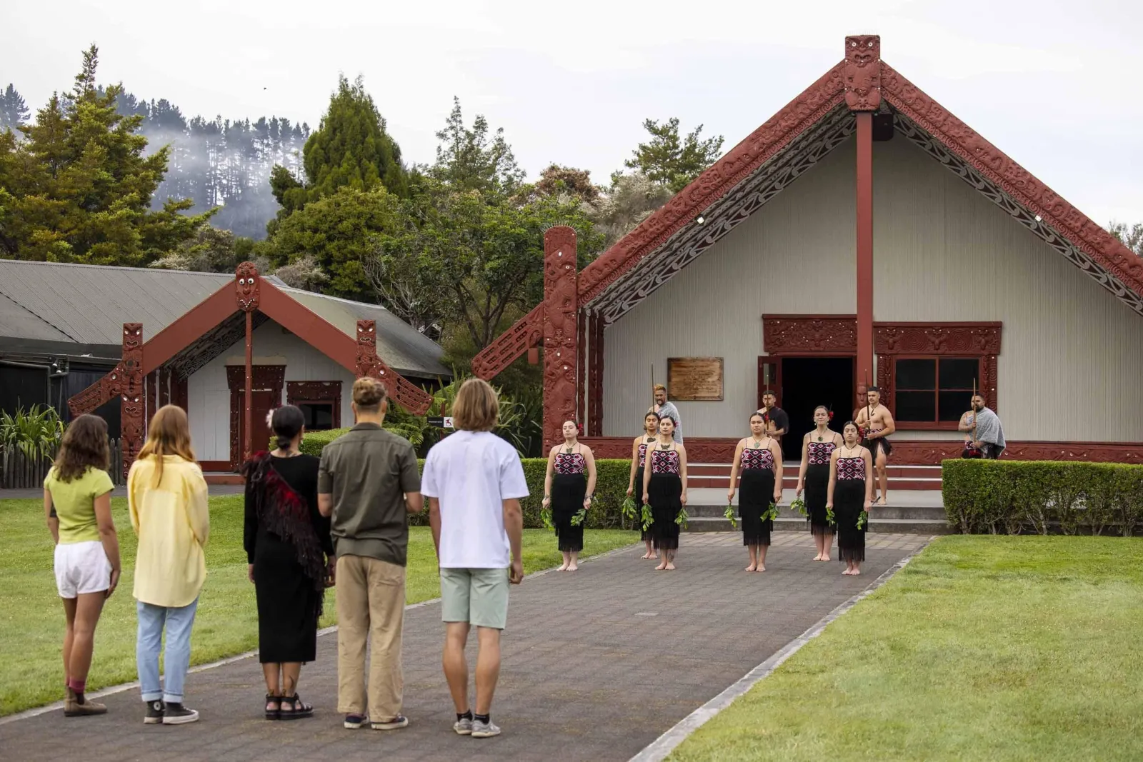 Visitors walking towards Te Puia's carved wharenui as performers wait on the steps