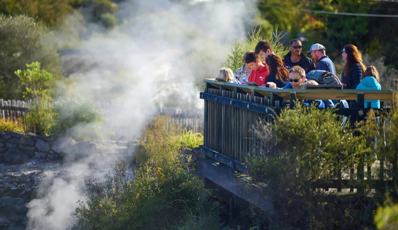 Visitors on a viewing platform above steam rising from a thermal pool